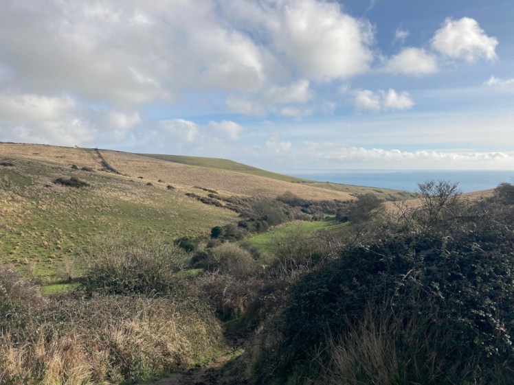 The view down Seacombe towards the sea as seen from the top of the hill - more rolling green hills but now there are clouds coming in.