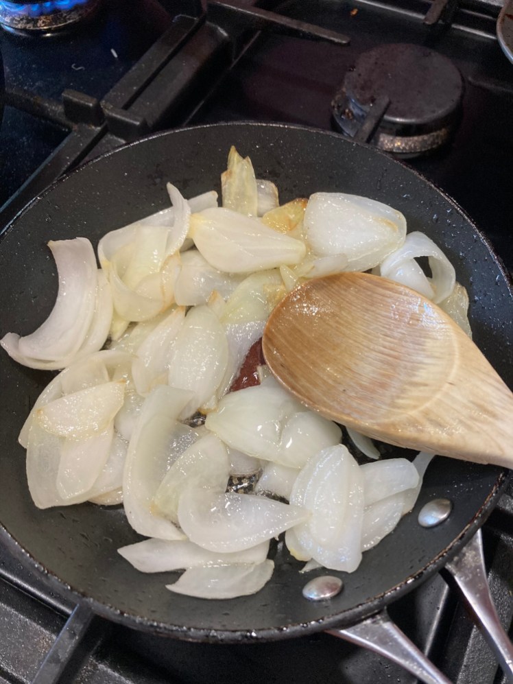 The home-grown onion chopped and being fried in a small pan.