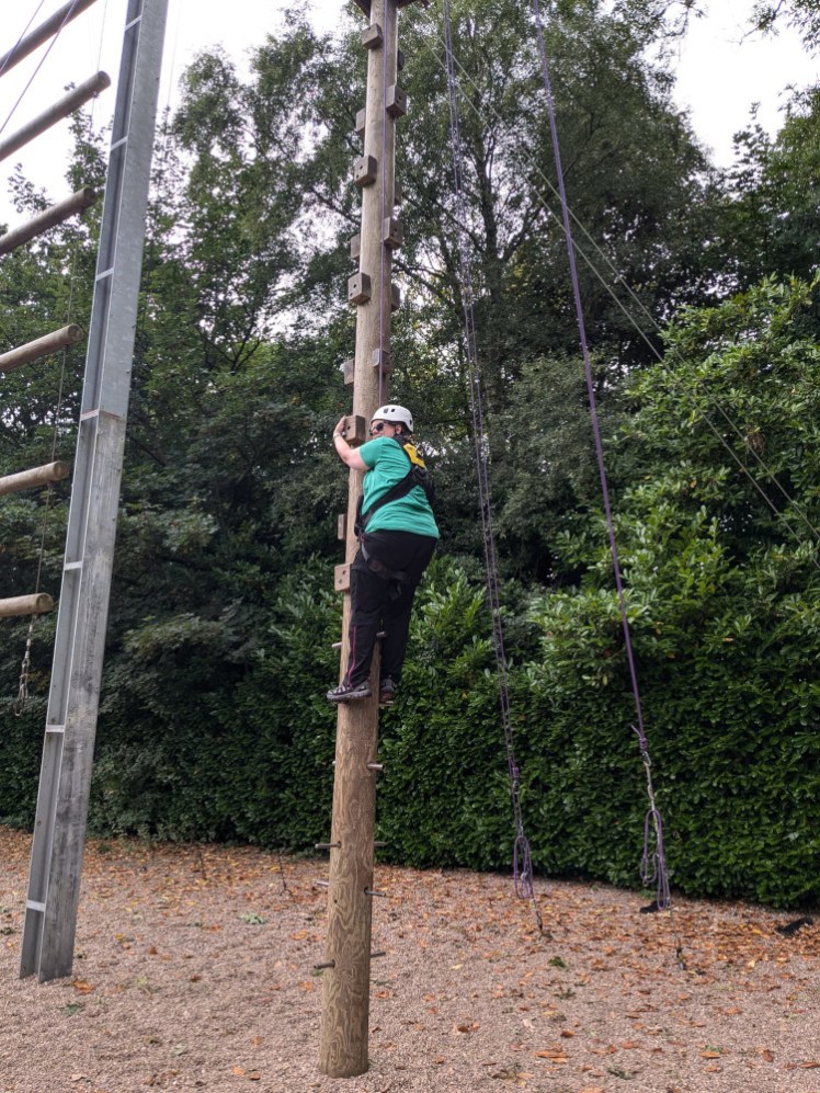 Me on High All Aboard, in a green t-shirt and full body harness. I'm standing on metal posts about six fee off the ground.