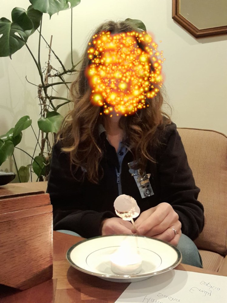 An anonymous leader with a face full of stars and long hair cooking a marshmallow over a tealight. The marshmallow is slightly burnt at the end.