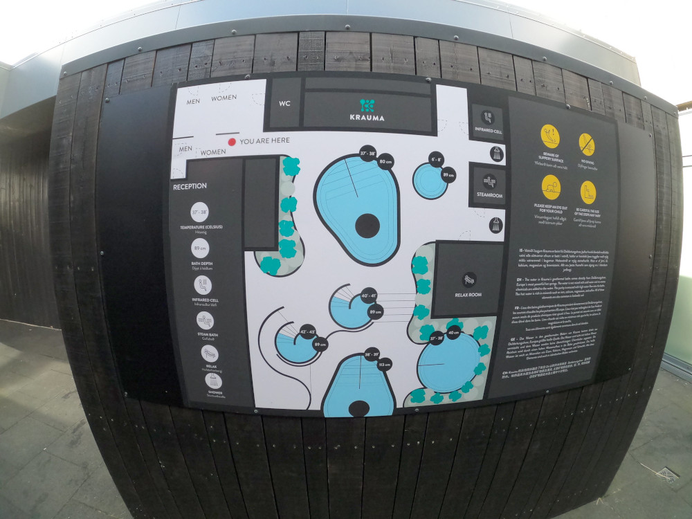 A map of Krauma's hotpots on a dark wooden wall. The photo is taken with my GoPro so the edges of the map are all curved. It shows six blue circles - well, four circles and two pear-shapes surrounded by an assortment of black squares which are the buildings.