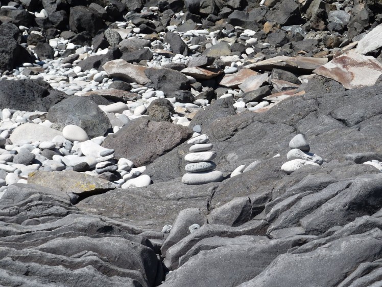 Rocky bit of shore littered with small towers of rounded grey pebbles by "original" and "artistic" tourists.