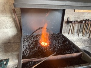 A lit coke forge. It's a large tray filled with black rocks and a fire in the middle. There's a back to it and a hood to suck away the fumes. At the front is a tray full of water for dipping your hot tools.