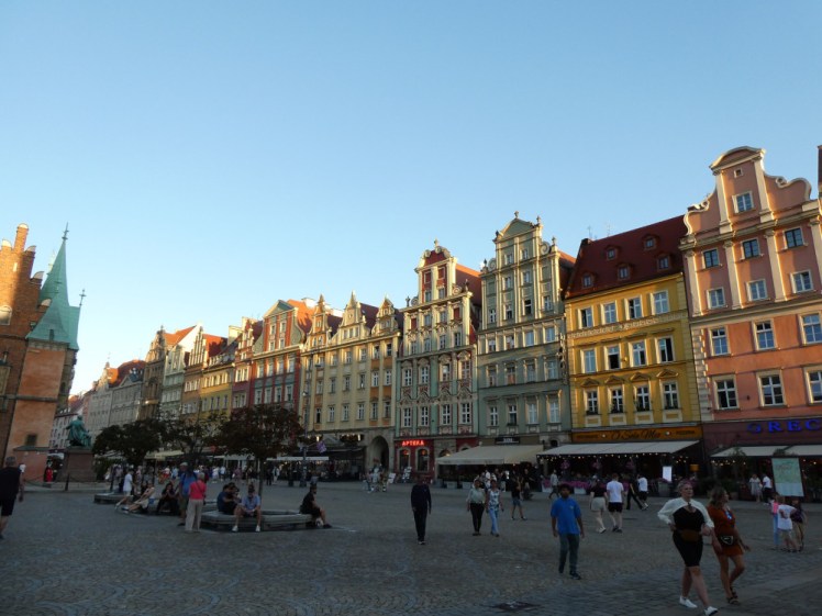 Old Market Square, Wroclaw, lots of yellow and green and pink buildings glowing golden in the evening sun.