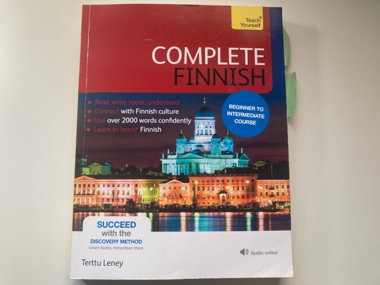 Teach Yourself Complete Finnish. A textbook with the title in a big red box occupying the top third. The rest is mostly taken up by a picture of Helsinki's white cathedral by night with various encouraging words about what the book can do for you dotted around.
