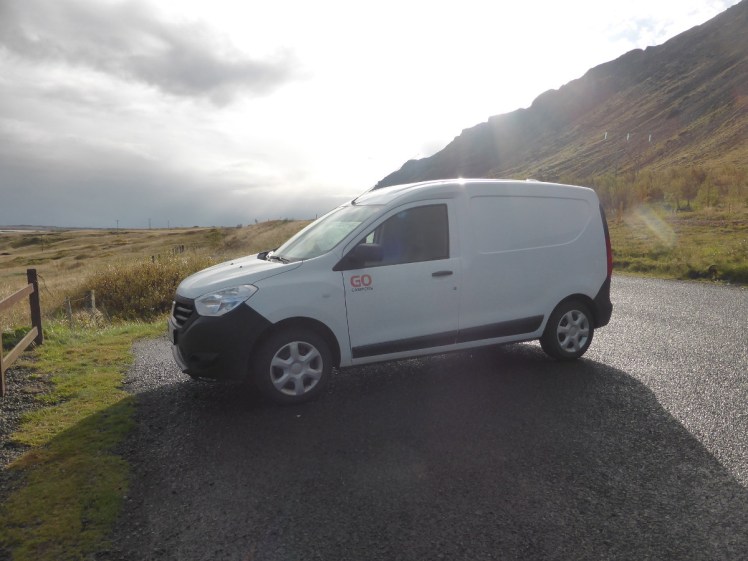 Campervan parked by the foot of a mountain with the low sun backlighting it