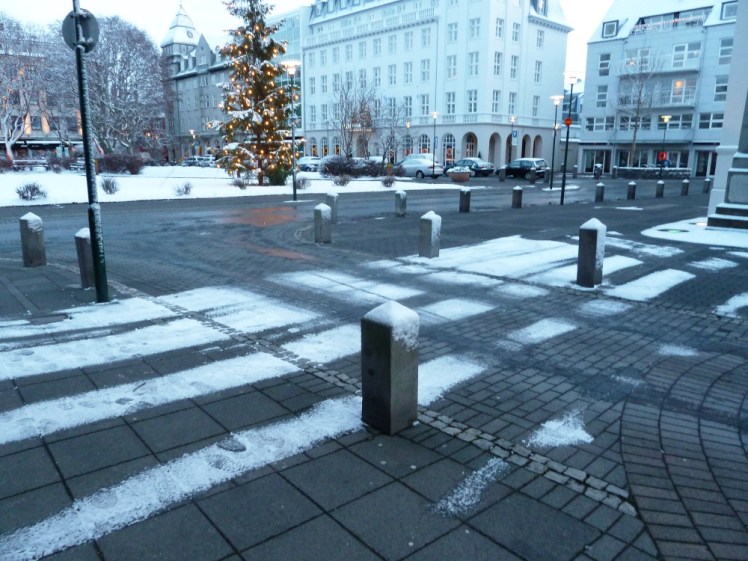A street in downtown Reykjavik. The pavement and square behind are covered in a light layer of snow but the road is clear because of the hot water pipes underneath.