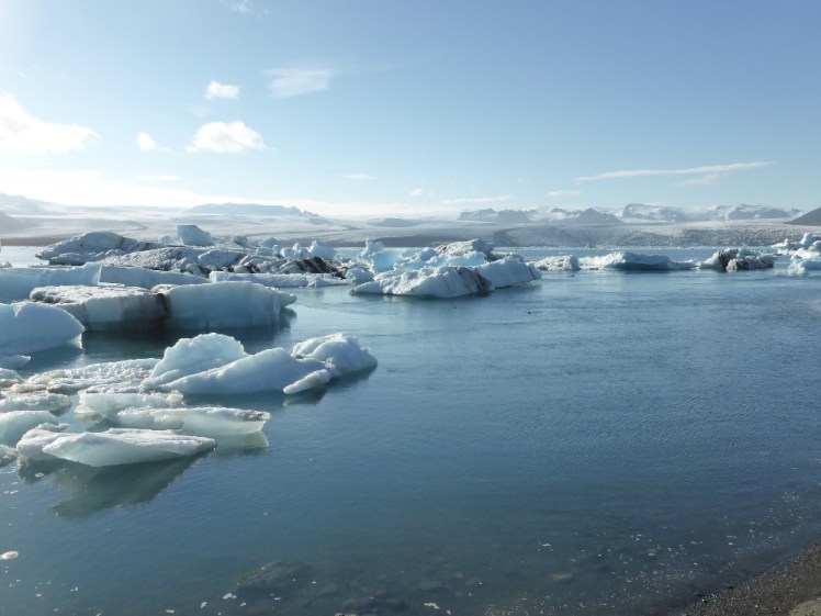 Striped blue icebergs floating in a blue lagoon under a blue sky.