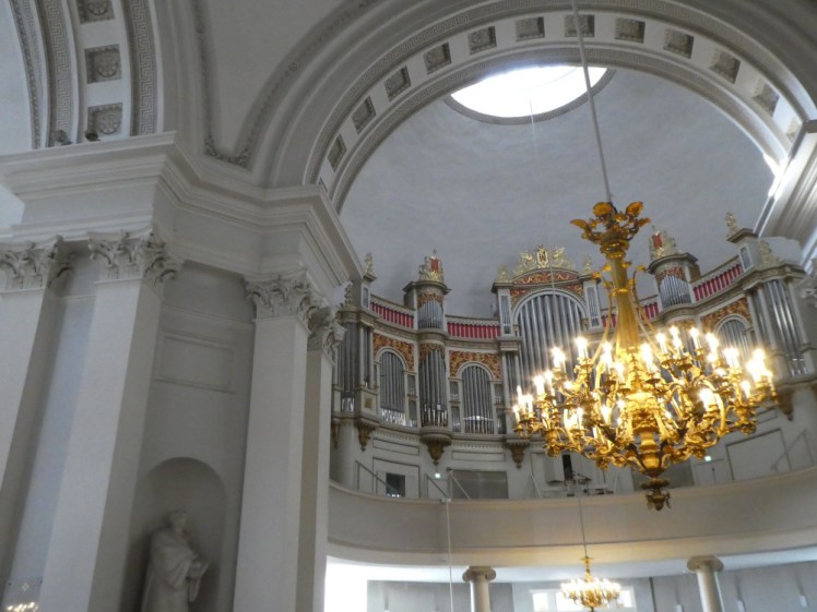 The interior of the cathedral. The walls and arches are painted a light grey-blue and there's a fairly spectacular gold chandelier hanging down.