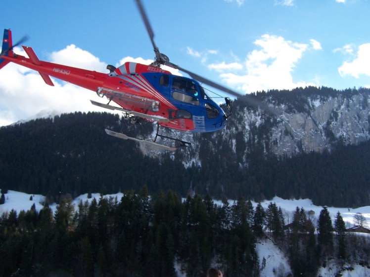 Eurocopter AS350 Ecureil helicopter - a small single-engine light helicopter that seats 5, in red and black Heli-TV livery, just taking off among snowy mountains.