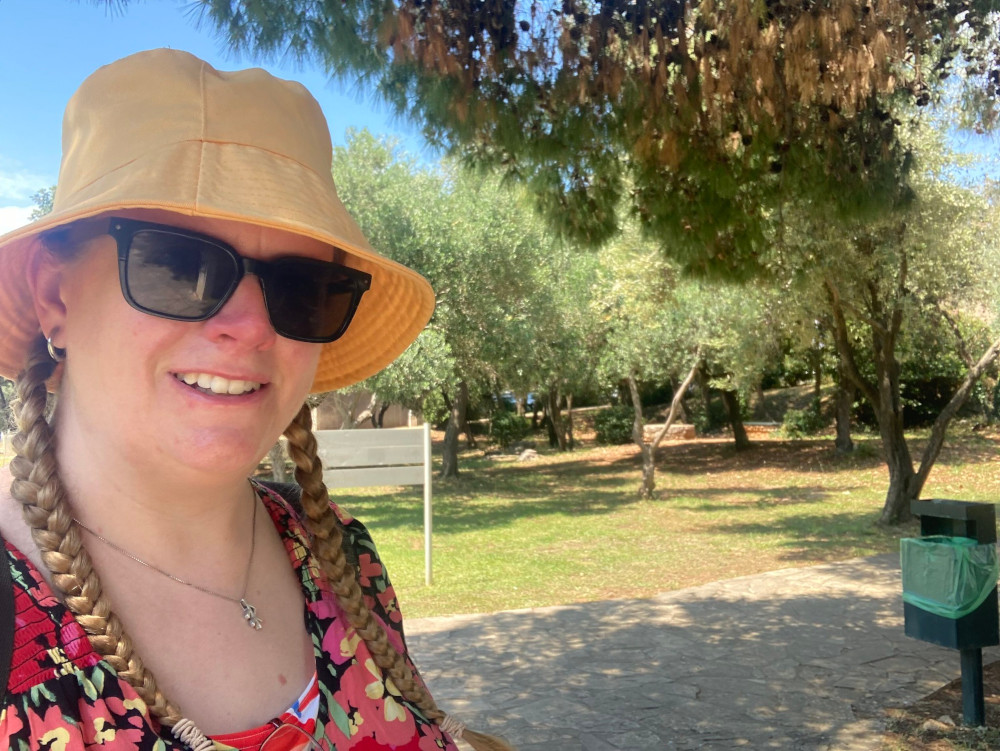 Me, in a yellow bucket hat and flowery dress on a path through a greenish park.