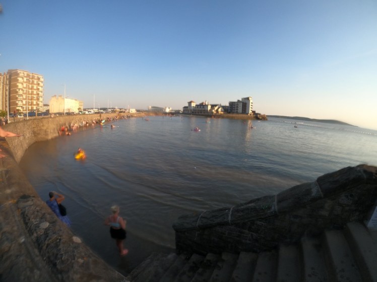 A bad fish-eye GoPro photo from the top of the landward wall showing steps going down to the walkway around the lake. The walkway is under water but it's shallow enough at the moment for plenty of people to still be standing there.