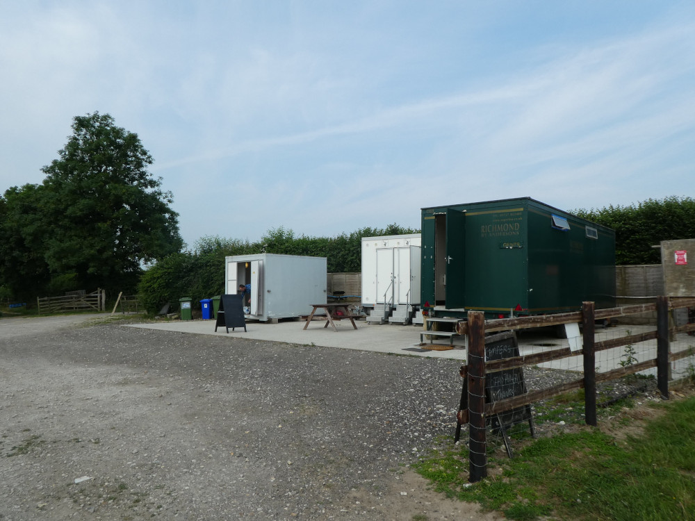 The campsite facilities - three temporary/portable containers. The washing-up area and showers are white and the toilet block is green and raised up on wheels.