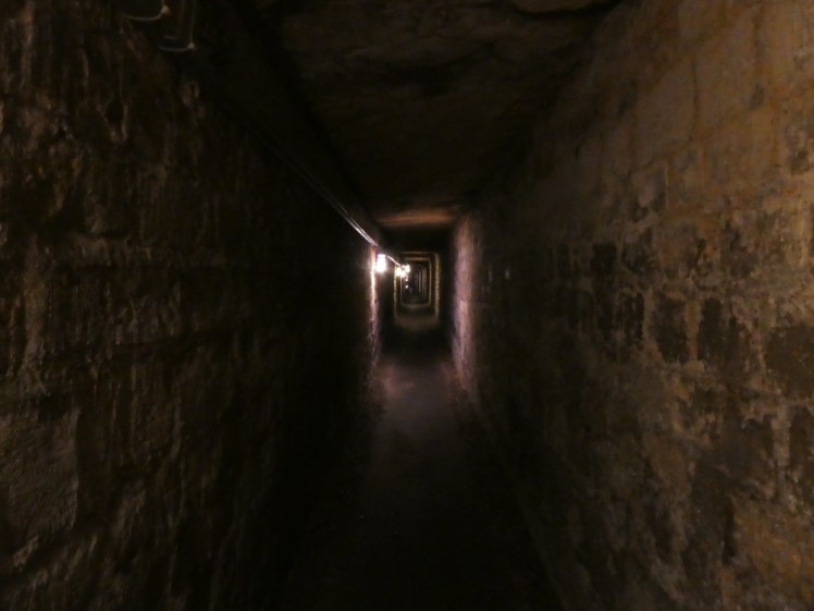 Empty mining gallery, rectangular, wide enough for two to walk comfortably and three to squeeze, lit on the left by a small light every fifty or so yards.