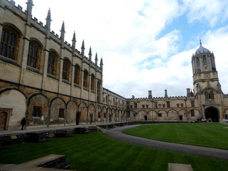 Yellow stone walls surround a central grassy quad. On the other side, a tower rises up.
