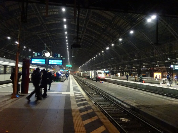 On platform 5 of Cologne Hauptbahnhof in the winter evening. A huge arched roof encloses the long station. There's a white ICE train at the next track but this one is empty.
