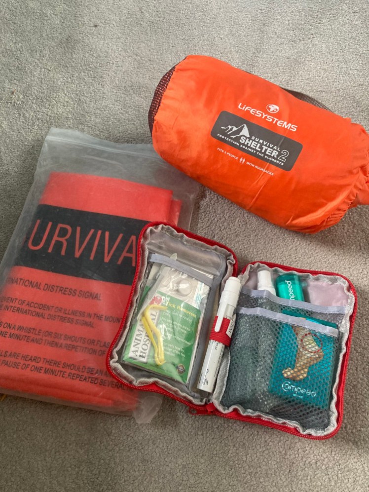 My emergency kit. At the top is a group shelter in a bag like a mini sleeping bag. On the left is an orange survival bag folded neatly into a large ziplock bag and to the right is my open first aid kit.