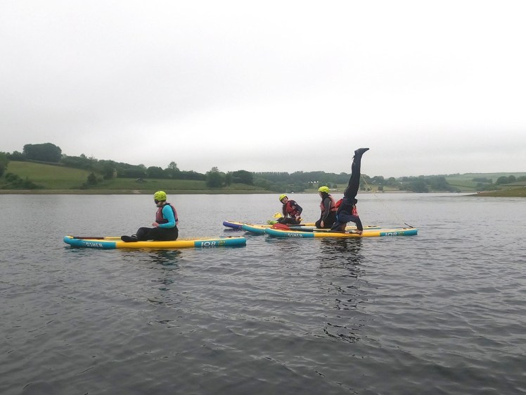 The group gathered around a corner of the lake. The instructor is standing on his head on his board.