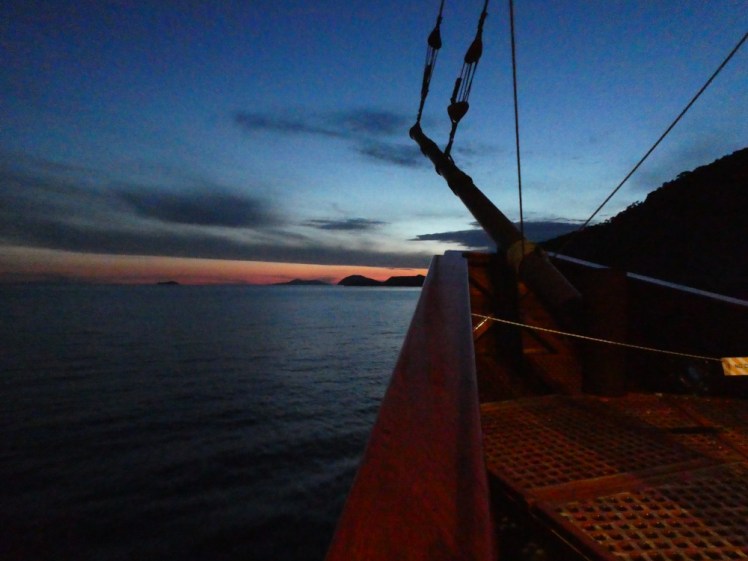 Fading red sunset ahead, with the lumps of the Elafiti Islands rising out of the water. In the foreground is the bow of the Karaka.