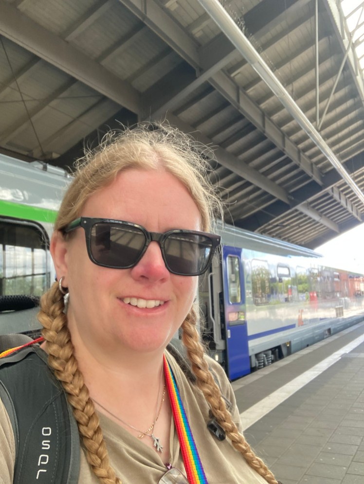 A selfie with the Polish intercity that I hoped would take me to Poznań. It's mostly light grey but the carriage behind me has a bright green line running near the top and the next one has a blue line and blue door.