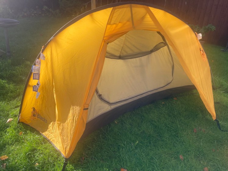 A one-man yellow tent with a long pole over the top. It's glowing in the November sun.