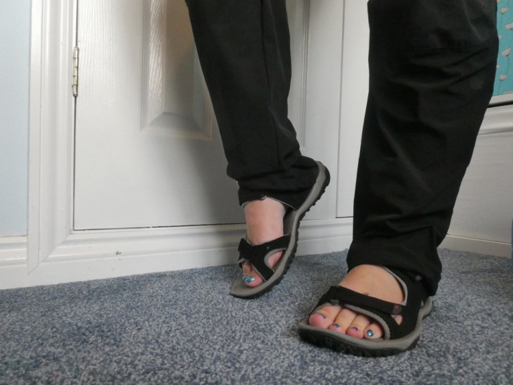 My legs and feet. My toenails are painted a bright metallic glittery blue. The sandals are low-profile ones with solid black straps across toes, forefoot and around heel.