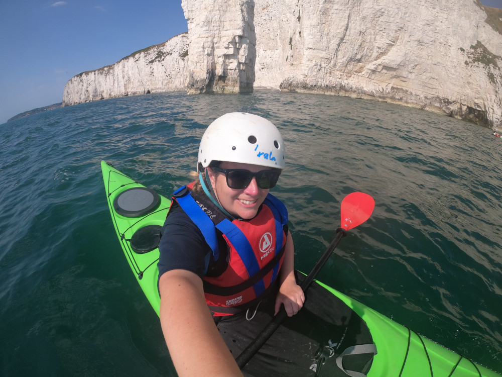A GoPro selfie in a bright green sea kayak. I'm wearing a white helmet and a red buoyancy aid over a navy t-shirt. The sea is calm and beautiful and behind me are chalk cliffs.