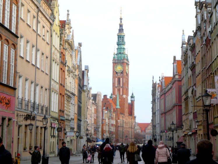The main tourist street of Gdansk, lined with pastel Hanseatic buildings and dominated by the Town Hall's tall thin tower.