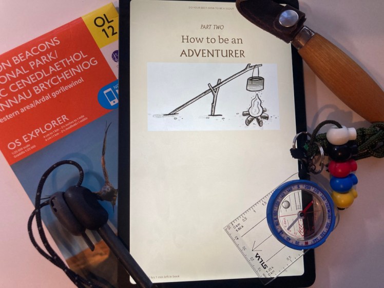 My tablet showing the chapter title page How To Be An Adventurer. The tablet is surrounded by an OS map, a firesteel, a curved spoon-carving knife and a compass.