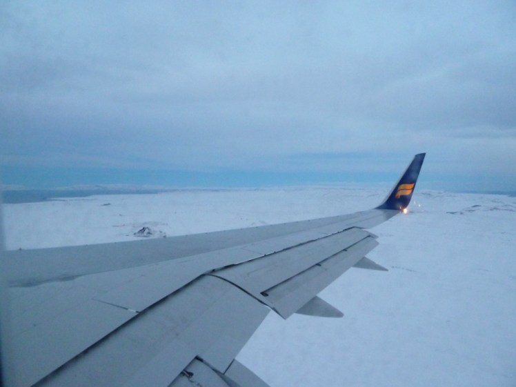 The wing of an Icelandair plane coming in low over Iceland which is well and truly iced and snowed over.