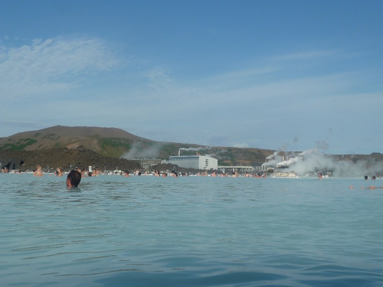 The famous blue waters of the Blue Lagoon, with a mountain in front. Between the lagoon and the mountain is the geothermal power station that provides the famous water.