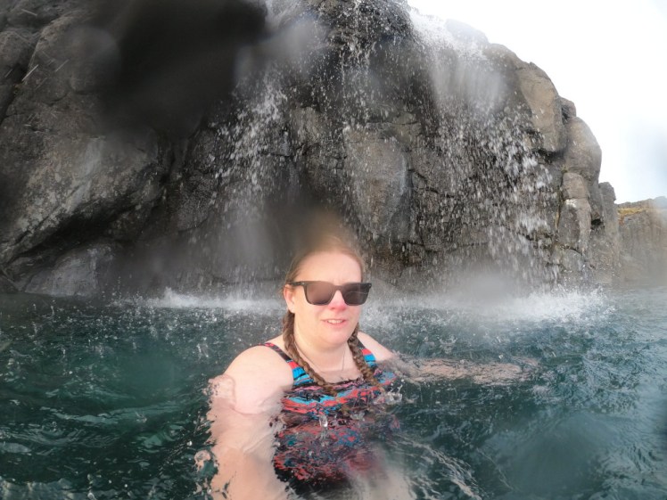 A selfie under the waterfall. There's a drop of water on the lens. The water is falling over the edge of the cliff at the north end of the lagoon.
