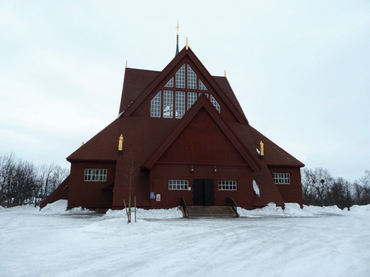 Kiruna Church, a kind of pyramid-shaped building in dark wood. The lowest of its roofs almost touches the snow.