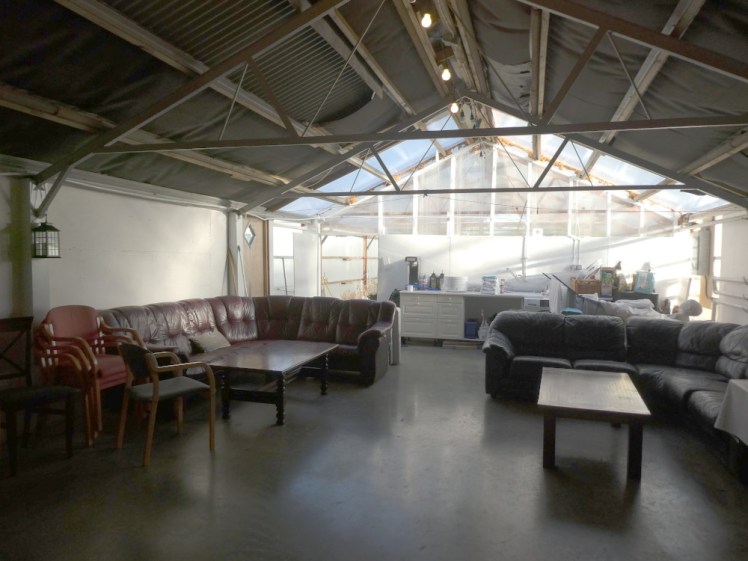 The communal room. It's full of tables, chairs and leather sofas. The far wall is glass and behind it is a greenhouse, which is actually the other half of the building.