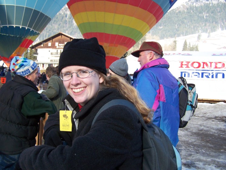 Me again, this time wearing a long dark grey wool coat, a plain black fleece hat and wearing a bright yellow label/ticket through my top buttonhole. Behind me there are three brightly-coloured tethered balloons and lots of people in coats and hats.
