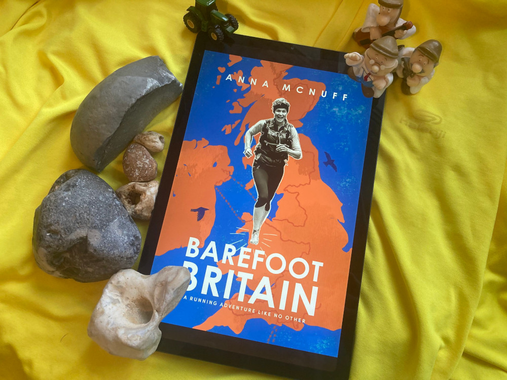 Barefood Britain by Anna McNuff on my tablet. The tablet is lying on a bright yellow running top. In the top corner is a tiny toy tractor and three of the Tetley Tea Folk. In the bottom corner, there's a collection of rocks from the British coastline.