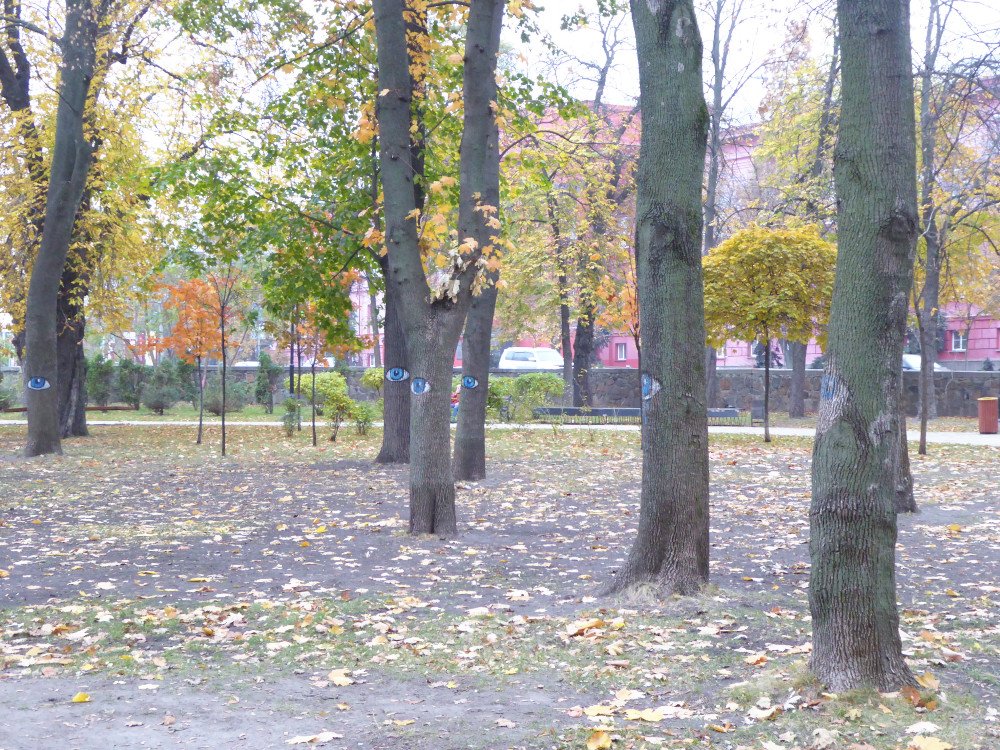 Trees in Taras Shevchenko Park. They each have a big blue staring eye painted at about eye-level on the trunk.