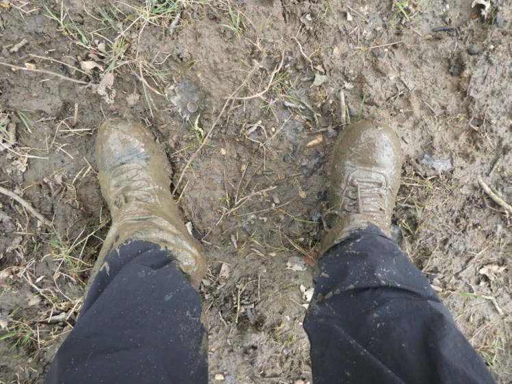 My boots and lower legs during a particularly muddy section of a March walk. The boots and my ankles are so covered in mud you can't tell what colour anything is meant to be. The ground isn't quite so muddy because I didn't stop for photos until I was clear of it but it's not exactly clean even now.