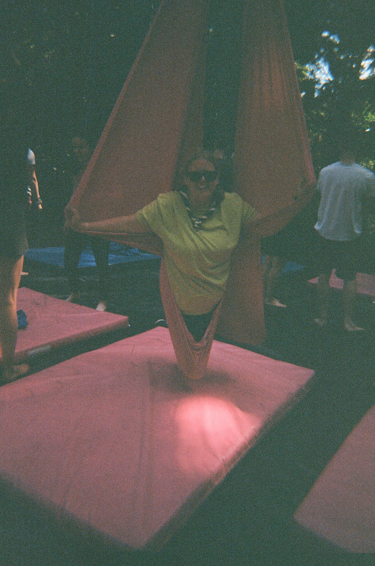 Me in a pink aerial sling, knees underneath me, arms held out like an angel. It's a bright summer day but this is under the trees and the camera hates it.