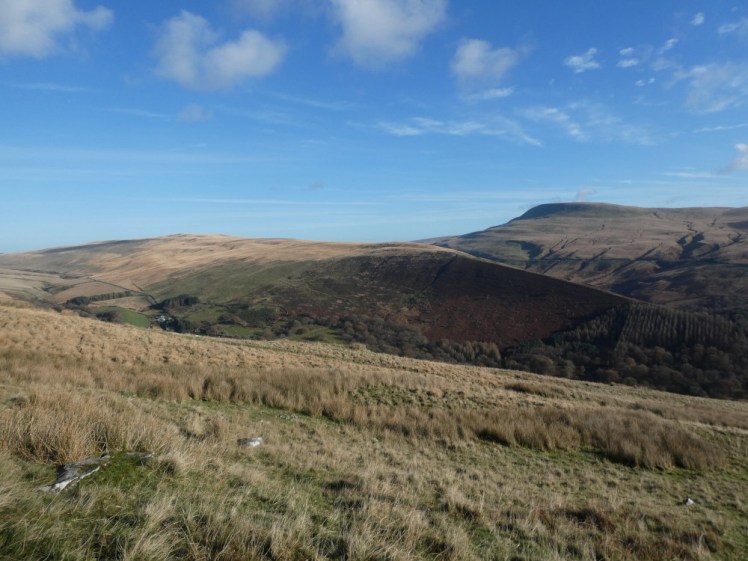 Fan Gyhirych, a mountain that's steep on one side and gentle on the other, as seen across rolling hills and mountains from the opposite side of the valley.
