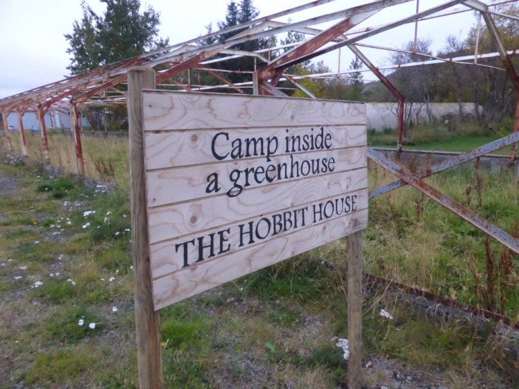 A wooden sign from 2017 saying "Camp inside a greenhouse - the hobbit house". This sign is now gone.