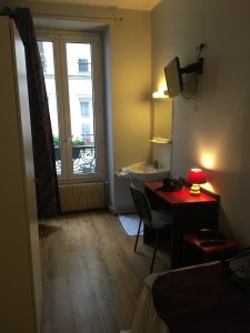 A dingy hotel room near Gare du Nord in Paris. It's a narrow room, lit only by a small lamp and a light over the sink. The door doesn't fit properly and it smells weird.