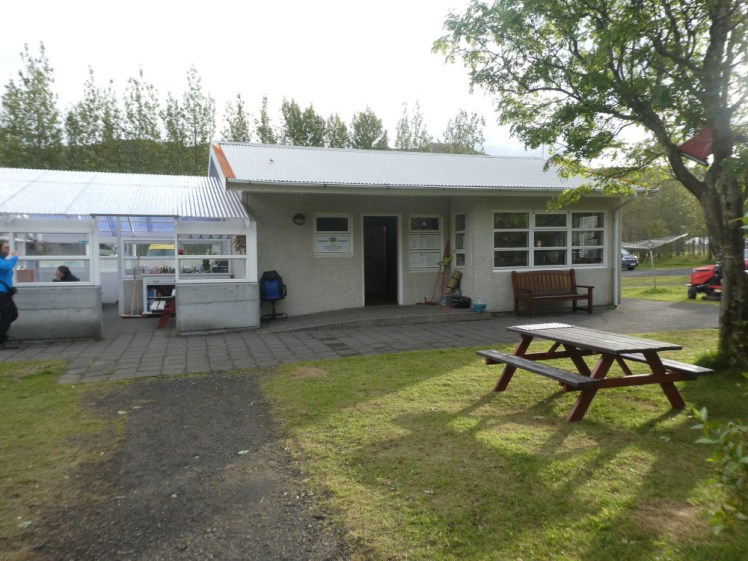 The kitchen and reception buildings in the morning sunshine. Opposite is a wooden picnic bench with a metal plate on it for cooking.