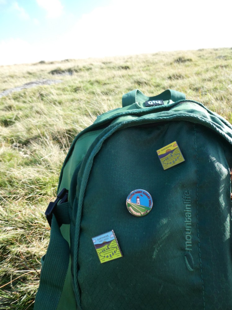 A close-up of the bag on the moor showing the front pocket and three pin badges pinned to it.