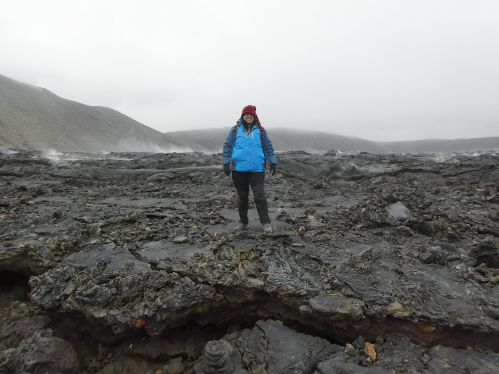 Me, in my red stripy hat and blue waterproof, standing on the edge of the lava. The steam is all well behind me and the front is wrinkled and crumbly and got some visible patches of green rock.