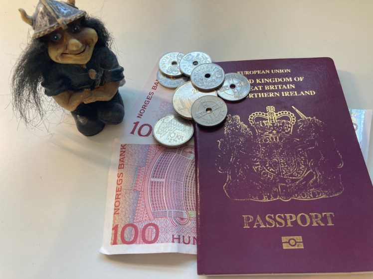 2 100NOK notes poking out from underneath my passport, with a small handful of silver Norwegian coins, many with holes in them, on top. Next to them is a grinning resin troll.