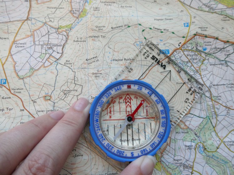 Taking a bearing: the compass lying on the map with its bezel turned to align north-south and the edge of the compass lined up between Saddle Tor and Haytor.