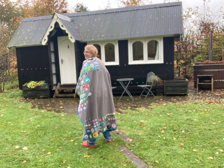 Me outside the tabernacle wearing a grey fleece blanket covered in badges. You can just make out jeans and red Crocs underneath.