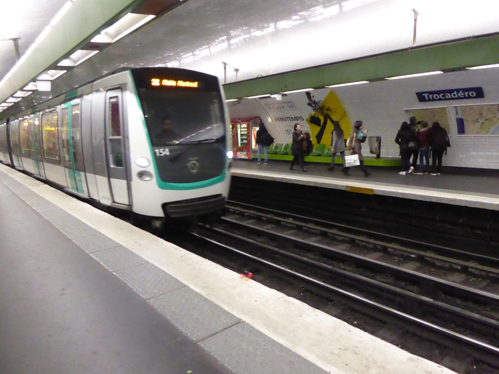 A white metro train with mint-green accents arriving at Trocadero station under Paris. It's all very well-lit and very clean-looking.