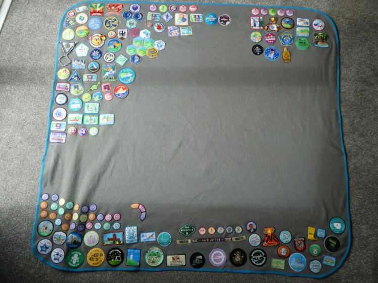 My new camp blanket, a grey fleece blanket with bright blue edging. This one has a lot of badges in the top-left corner and along the bottom, with a handful in the top-right. Most of the middle is pretty bare at the moment.